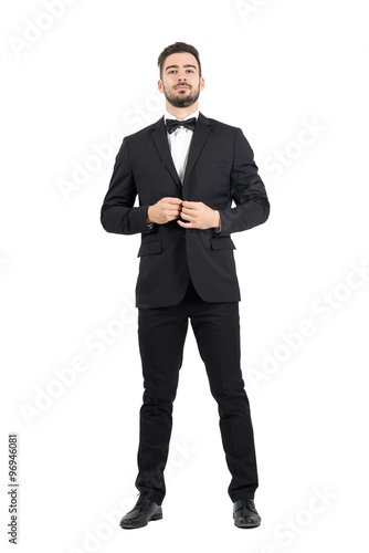 Young bearded wealthy man buttoning tuxedo with bow tie. Full body length portrait isolated over white studio background. photo