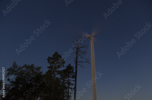 Some trees and a wind turbine with a star filled sky