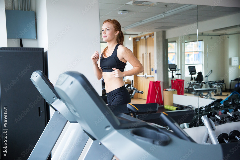 Pretty woman with red hair running on treadmill in gym Pretty woman with red hair running on treadmill in gym