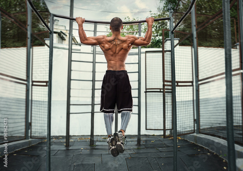  athlete doing pull-up on horizontal bar.Mans fitness outdoor photo