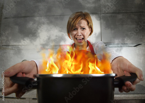 Foto young inexperienced home cook woman in panic with apron holding pot burning in f