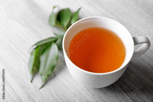 Ceramic cup of tea with green leaves on light wooden background