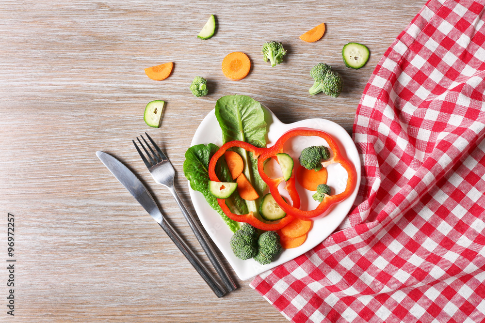 Useful cut vegetables on a plate in the form of heart on wooden table top view Useful cut vegetables on a plate in the form of heart on wooden table top view