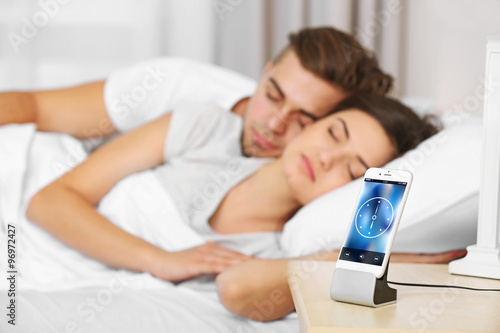 Happy couple waking up with mobile alarm clock