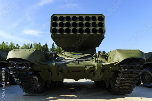 Multiple missile launcher, military industry, heavy mobile flamethrower system among two armored personnel carriers, green thermobaric ballistic weapon complex, modern army, blue sky on background  photo