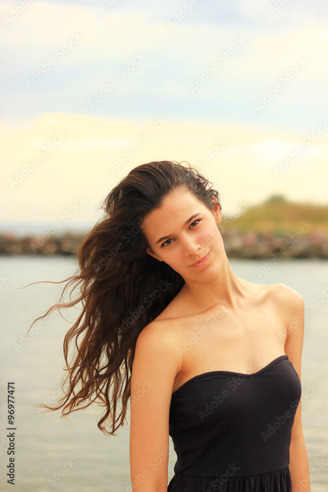 Beautiful slim brunette girl model posing in fashion dress by the sea, outdoor portrait. Natural look Beautiful slim brunette girl model posing in fashion dress by the sea, outdoor portrait. Natural look