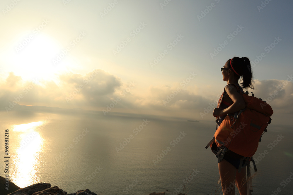 young woman backpacker at sunrise seaside mountain peak