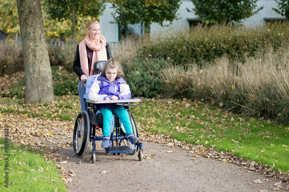 Disabled child in a wheelchair relaxing outside with help from a care assistant / Disabled child in a wheelchair relaxing outside together with a carer Disabled child in a wheelchair relaxing outside with help from a care assistant / Disabled child in a wheelchair relaxing outside together with a carer