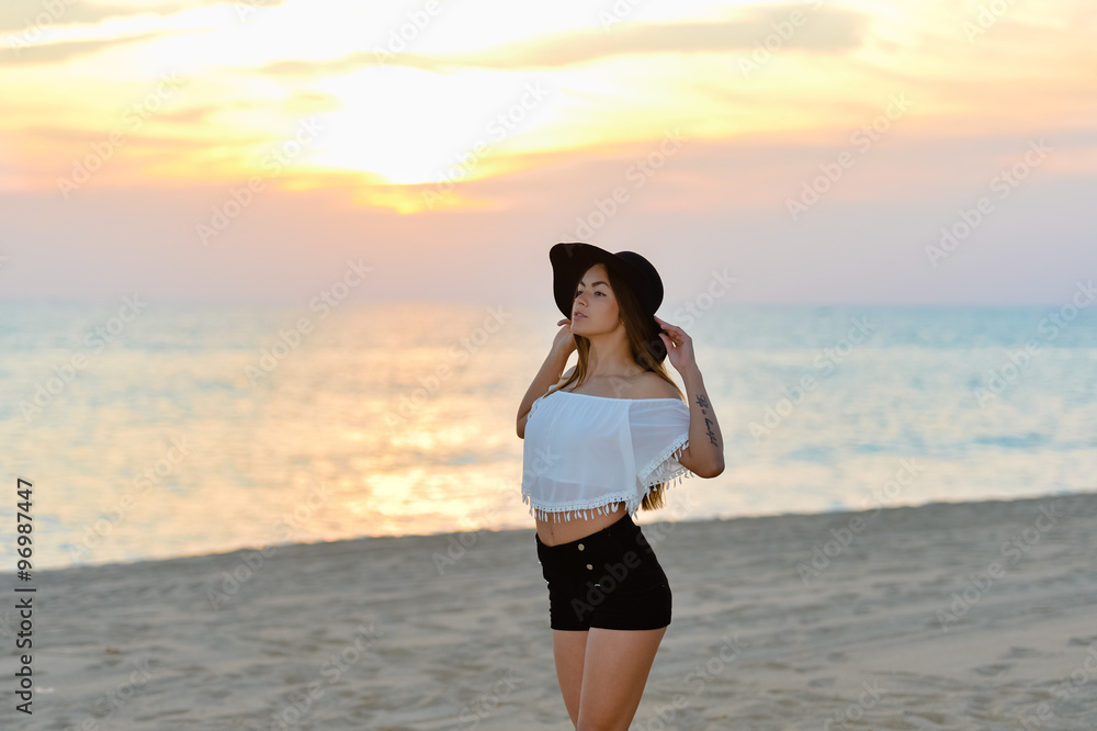 Pretty girl in black hat and shirts on sunset beach
