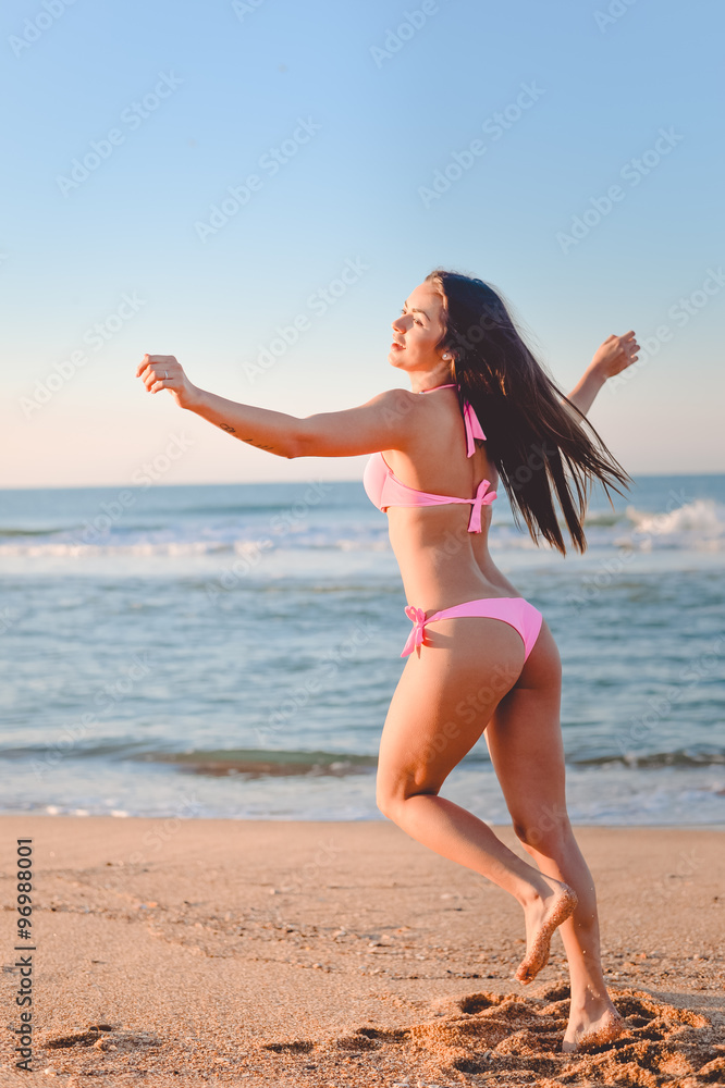 Naklejka premium Pretty girl in pink bikini dancing on sunny seaside beach