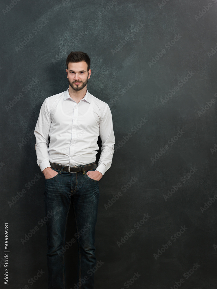 Portrait of a serious young man standing against green chalkboar