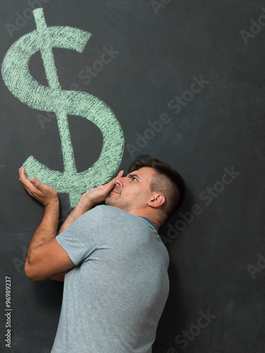 Happy  man standing in front of dollar sign written on a chalkbo photo