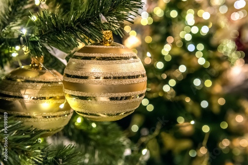 Two gold balls are on the christmas tree. Gold-green background with bokeh.