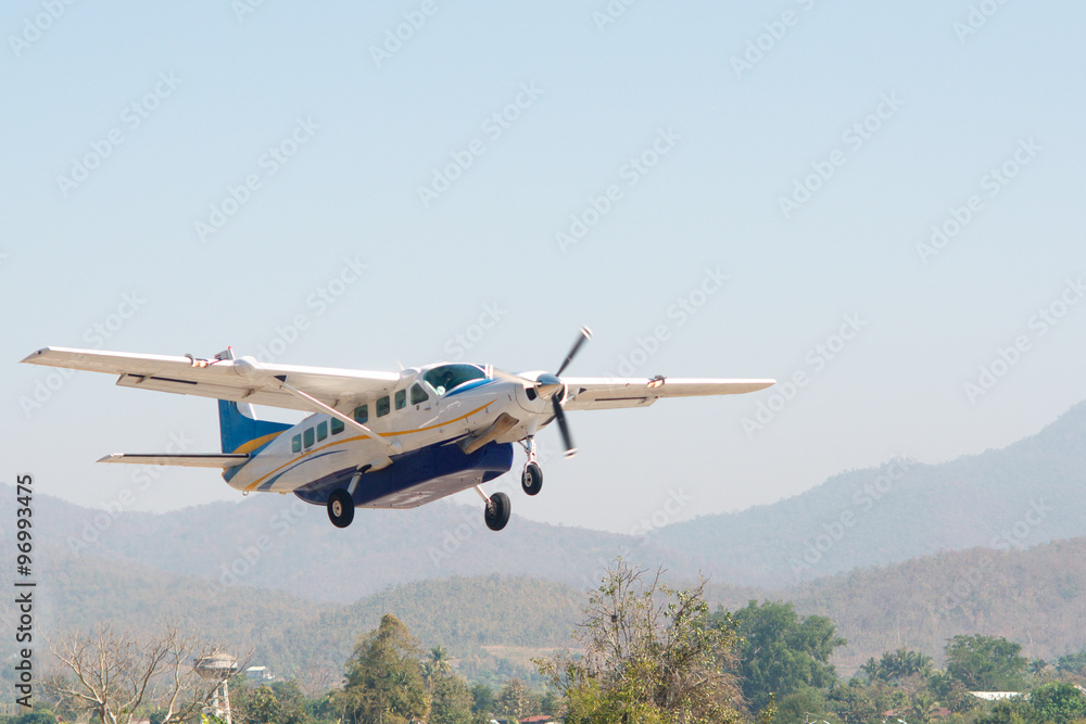 Small blue and white plane taking off with mountains in backgrou Small blue and white plane taking off with mountains in backgrou