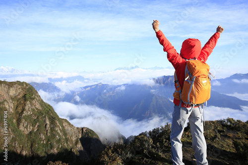 cheering young woman hiker open arms at mountain peak