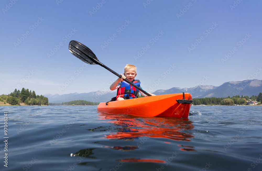 Young Boy paddling a kayak on a beautiful mountain lake. Low angle view of the nature's beauty