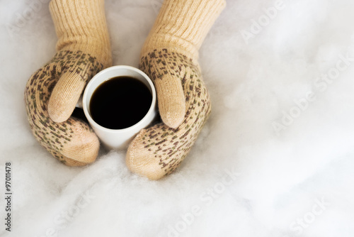Woman hands in teal gloves are holding a mug with hot coffee or