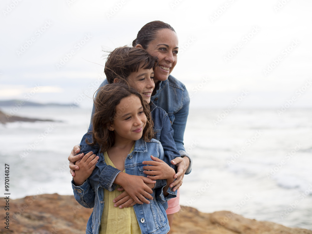 Madre abrazando a sus hijos junto al mar