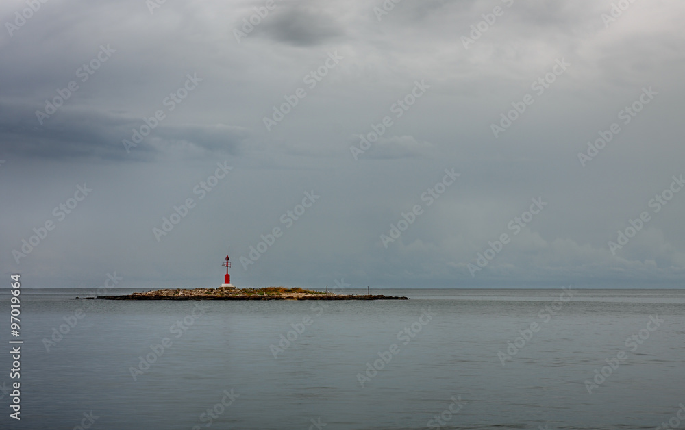 Fototapeta premium Red lighthouse on small island, on background cloudy sky.