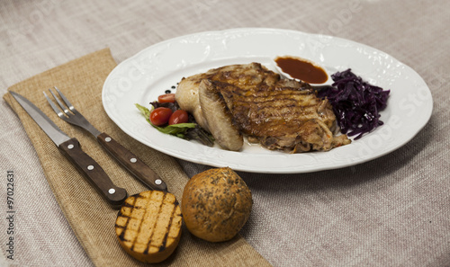 Juicy roast chicken with vegetables and ketchup. Served on porcelain plate on a tablecloth with fork and knife . Fried chicken tapaka, tobacco. photo