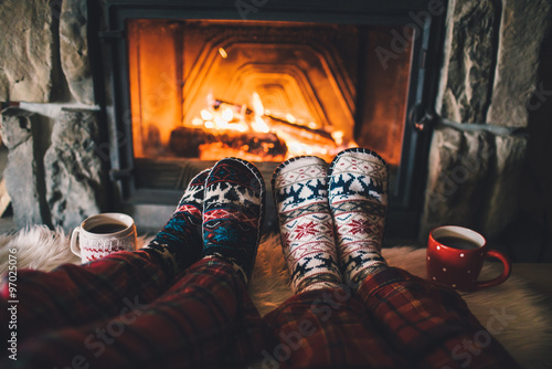 Feet in woollen socks by the Christmas fireplace. Family sitting relaxes by cozy authentic fireside with a cup of hot drink and warming up their feet. Winter and Christmas holidays concept photo