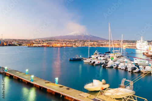 Fotografie, Obraz Skyline of Catania and its harbor with snowy volcano Etna in background after th