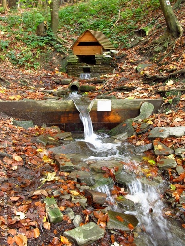wooden well and spring flowing from it on the rocky slope in the mountains in autumn