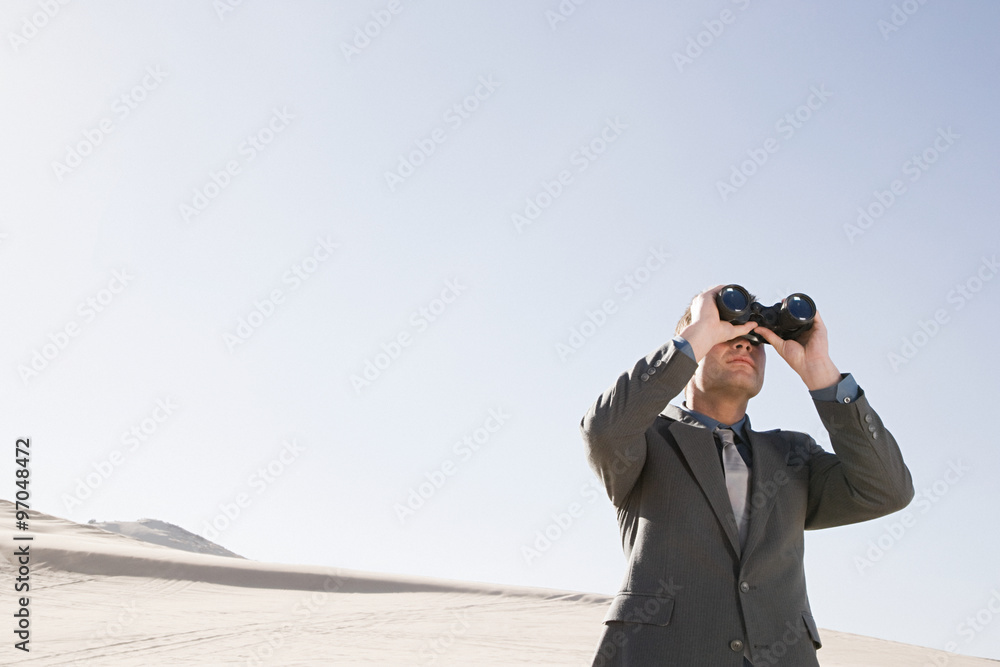 Businessman in desert with binoculars Businessman in desert with binoculars