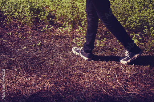 Feet in sneakers walking in the forest. Vintage tone.