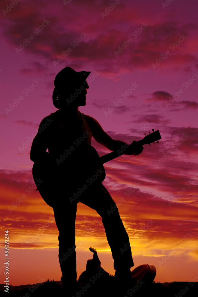 silhouette of a cowboy foot on saddle playing guitar