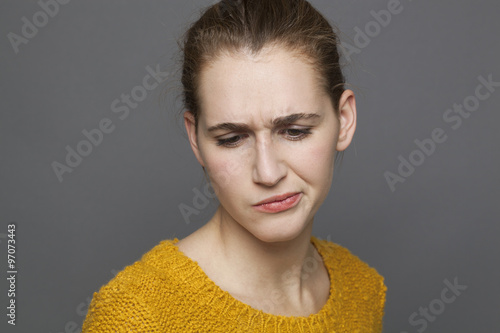 negative feelings concept - portrait of dubious beautiful 20s girl expressing suspicion and sadness,studio shot on gray background