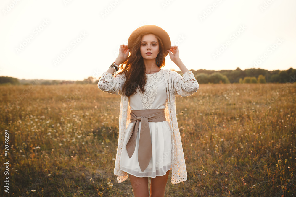 Fashion portrait of beautiful young pretty girl with hippie outfit holding  hat outdoors at sunset. Soft warm vintage color tone. Boho lifestyle.  Bohemian Style. Horizontal with blank space for text Stock Photo