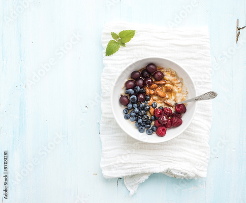 Healthy breakfast set. Bowl of oat porridge with fresh berries, almond and honey over white napkin. Top view, light blue backdrop