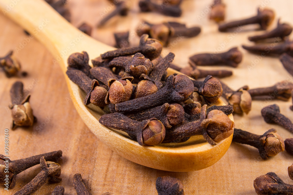 Heap of cloves with wooden spoon on table, seasoning for cooking Heap of cloves with wooden spoon on table, seasoning for cooking