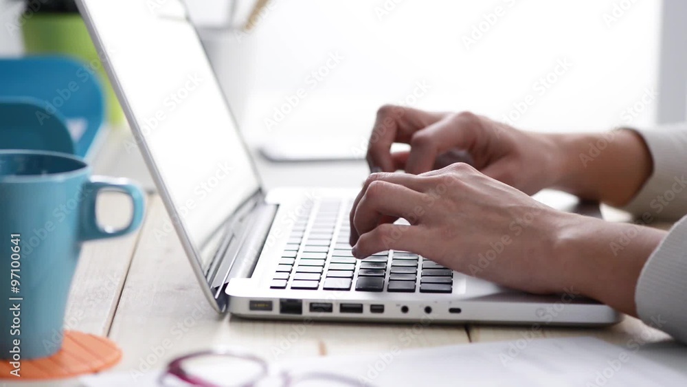 Young woman working at office desk, typing on laptop and smiling at camera, hands and eyes close up Young woman working at office desk, typing on laptop and smiling at camera, hands and eyes close up