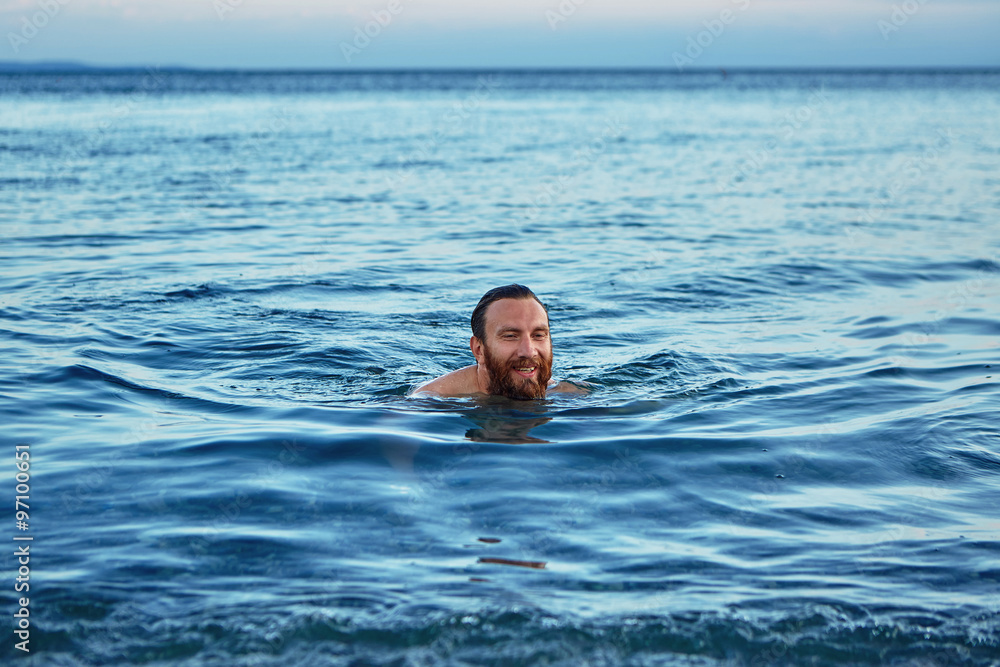 smiling man swims in the sea at dawn