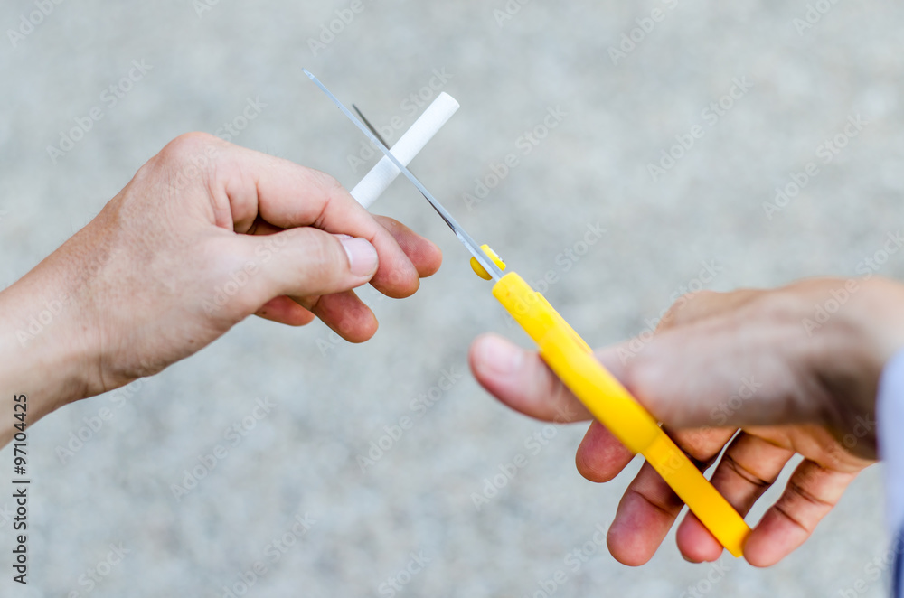 A hand hold cigarette being cut with scissors A hand hold cigarette being cut with scissors