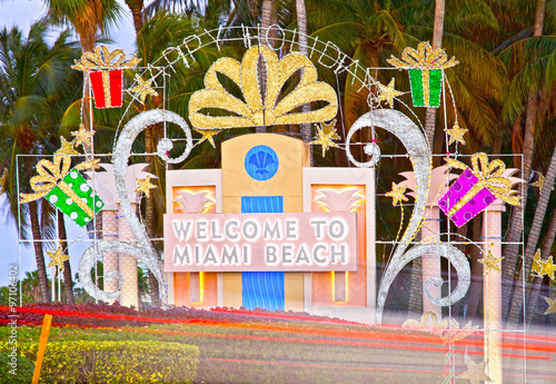 Miami Beach Welcome sign in Christmas holiday decorations and palm trees at sunset with moving traffic