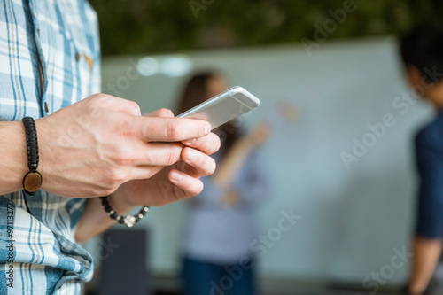 Hands of young guy using smartphone while his colleagues working