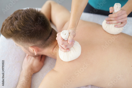 mann genießt eine massage mit kräuterstempeln