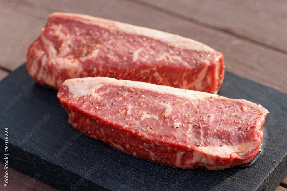 Two pieces of raw striploin steak on wooden plank