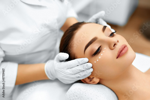 Skin Care. Close-up Of Cosmetician Applying Cosmetic Moisturizer Cream On Young Woman's Face. Beauty Face. Spa Treatment At Beauty Salon. Facial Beauty Treatment.