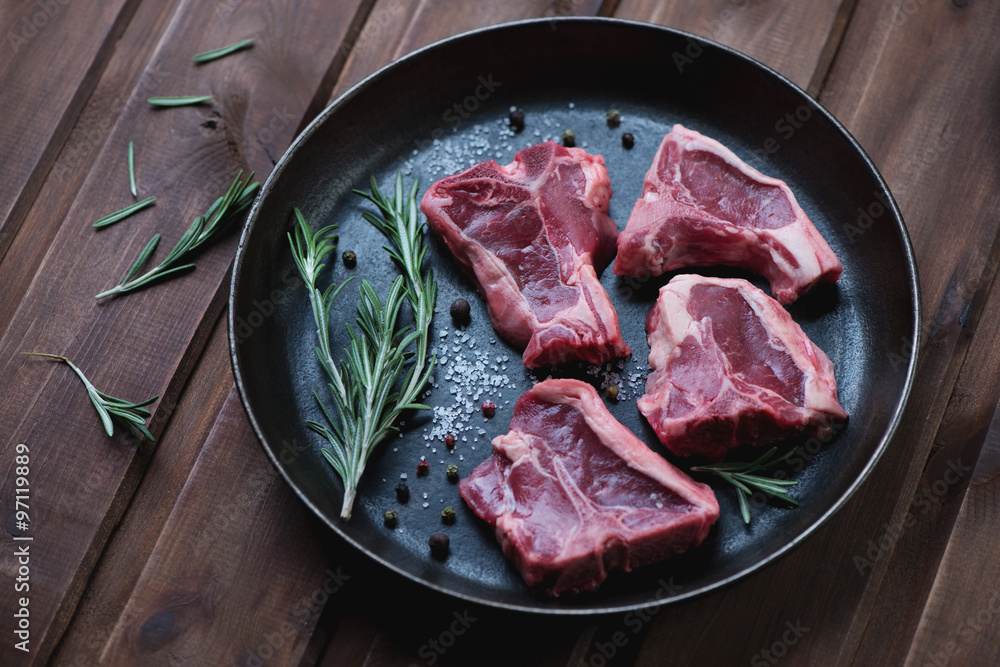Frying pan with uncooked T-bone lamb steaks and rosemary