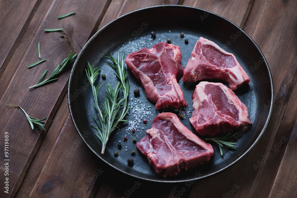 Frying pan with uncooked T-bone lamb steaks and rosemary Frying pan with uncooked T-bone lamb steaks and rosemary