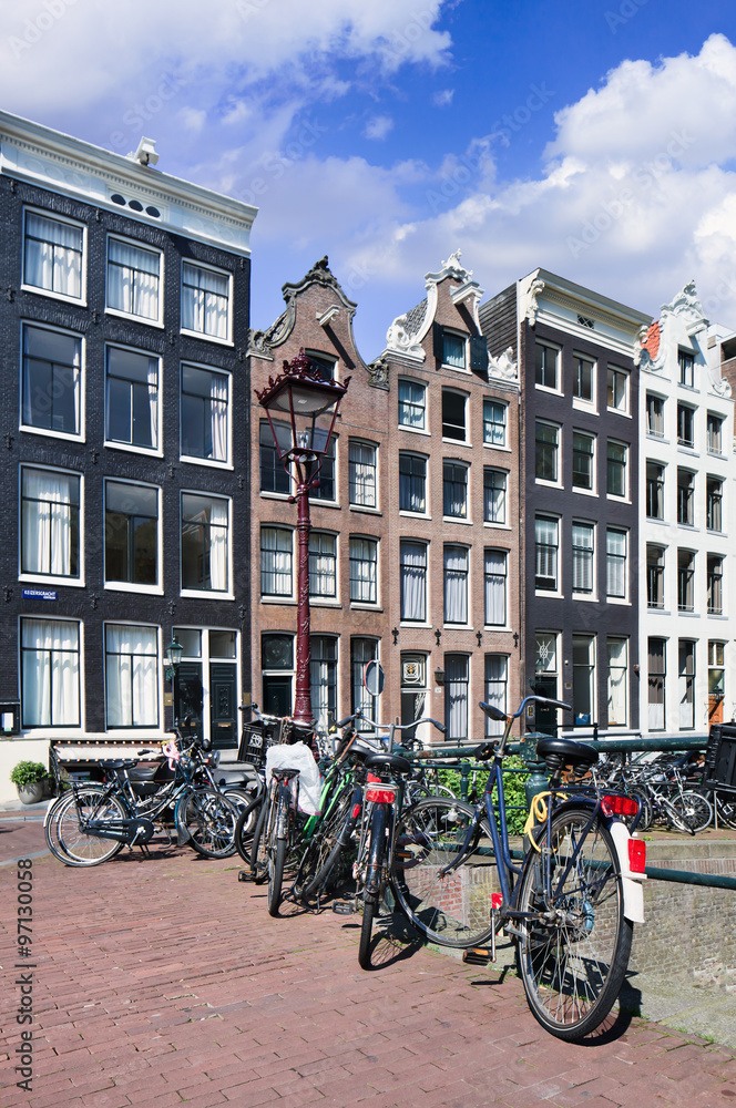 Bicycles parked against a rail with renovated ancient mansions on the background, Amsterdam, The Netherlands.