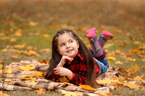 Happy young girl lying on plaid in autumn park