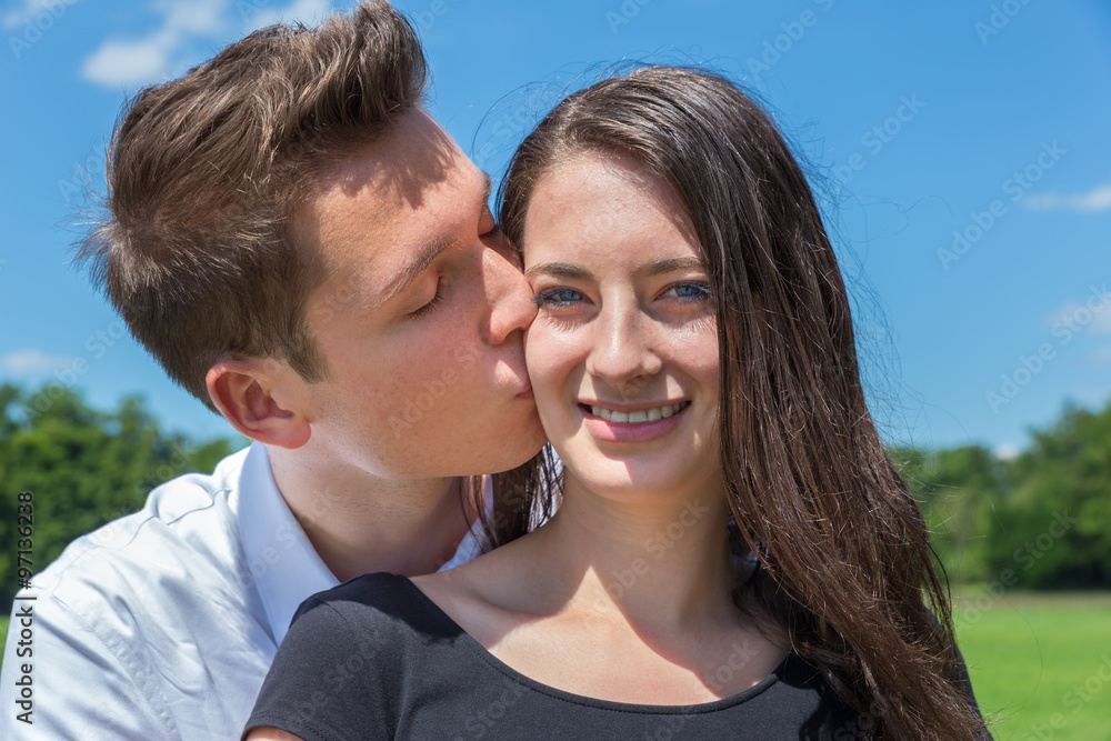 Boyfriend kisses girlfriend on cheek in sunny nature Boyfriend kisses girlfriend on cheek in sunny nature