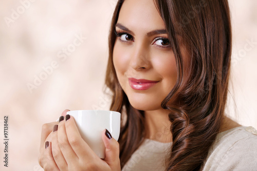 Portrait of smiling pretty woman with cup of coffee on pink blurred background
