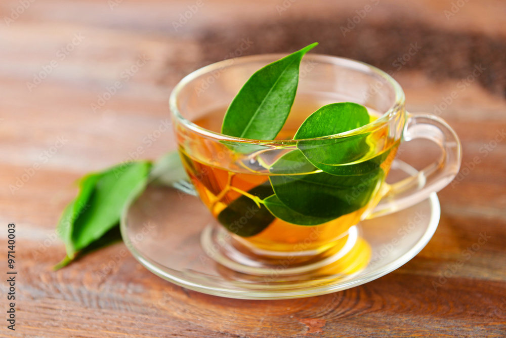 Glass cup of tea with green leaves on wooden background Glass cup of tea with green leaves on wooden background