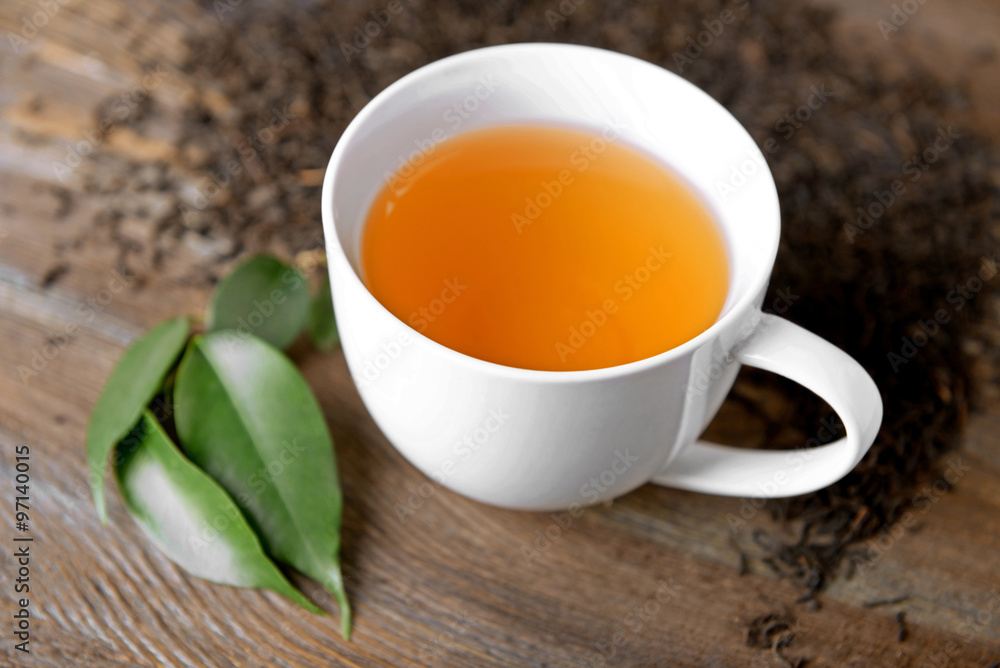 Ceramic cup of tea with scattered tea leaves around on wooden background Ceramic cup of tea with scattered tea leaves around on wooden background